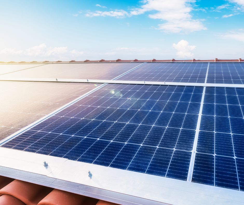 Paneles solares fotovoltaicos instalados sobre un tejado de tejas, captando la luz solar bajo un cielo azul con algunas nubes.